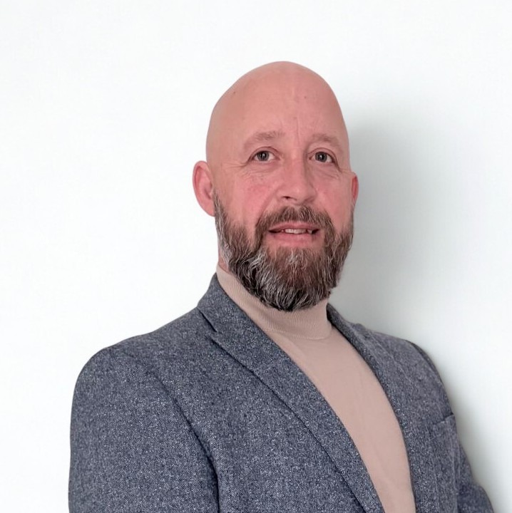 Phil Smith, smiling, wearing a tweed jacket over a roll-neck jumper