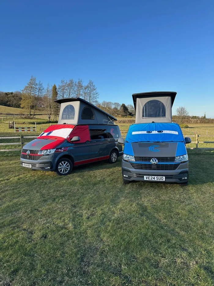 Enola and Fenyx parked side by side on grass with their pop-top roofs raised