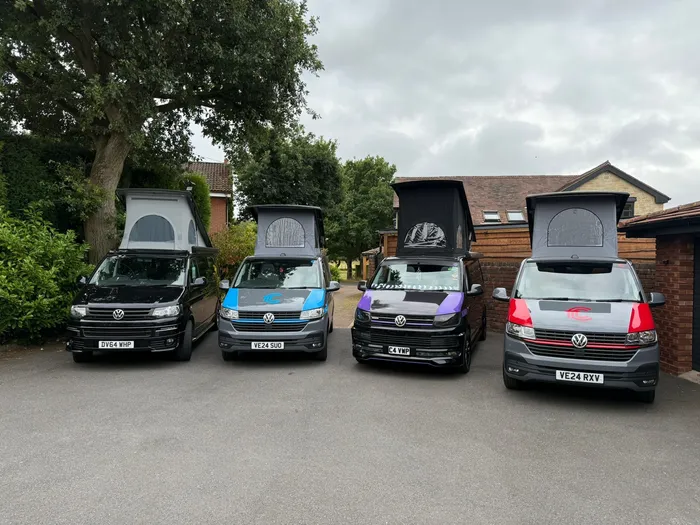 Four T.C. Campers VW campervans parked in a row with their pop-top roofs raised