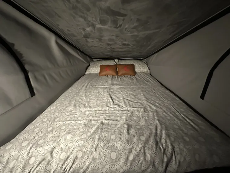 A double bed made up in the pop-top roof, with patterned bedding and branded cushions