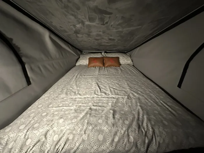 A double bed made up in the pop-top roof, with patterned bedding and branded cushions