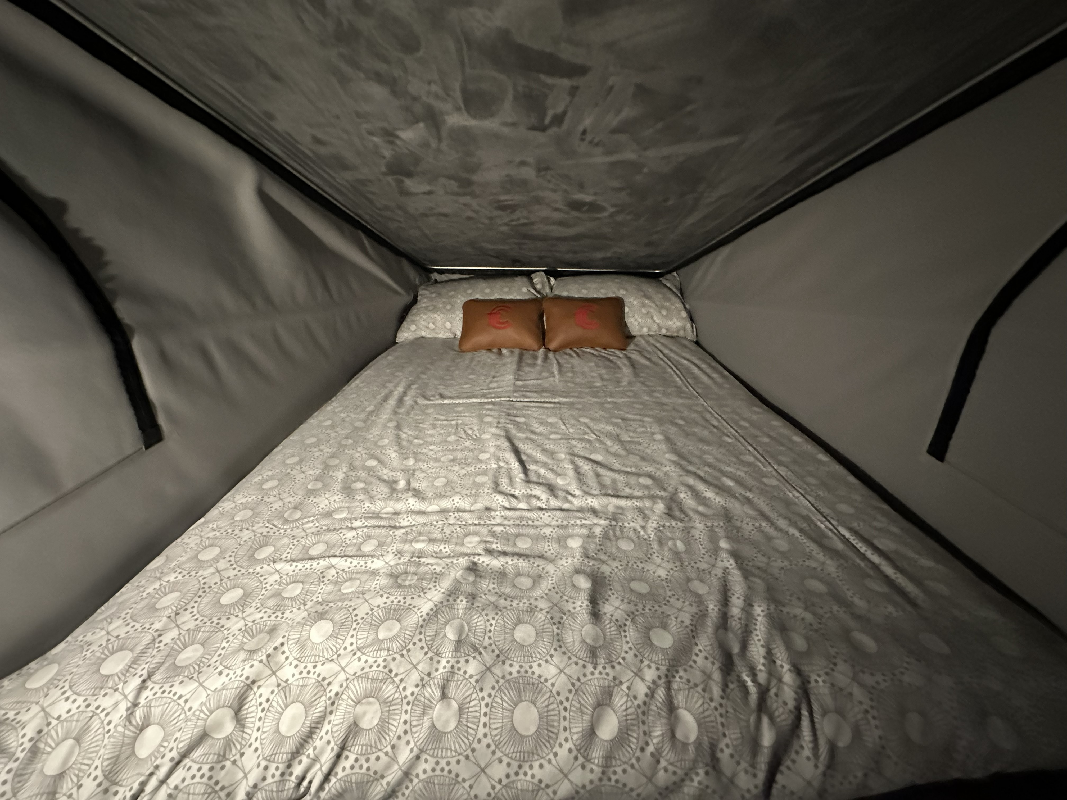 A double bed made up in the pop-top roof, with patterned bedding and branded cushions